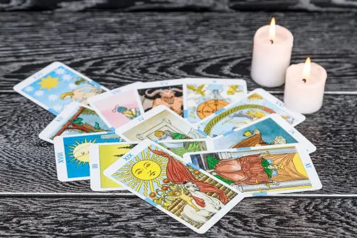 A Tarot deck spread out on a table with two candles with the major arcana cards in a spread out pile