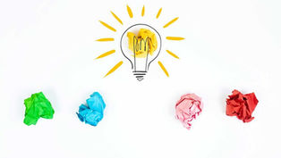 A light bulb with bright yellow light surrounded by colourful balled up pieces of paper