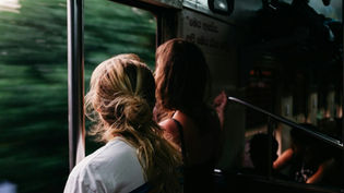 Two women looking out a train window as greenery rushes past