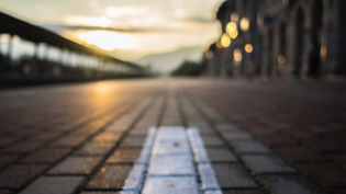 A large white arrow pointing toward the viewer on a city street with streetscape lit by morning light behind.