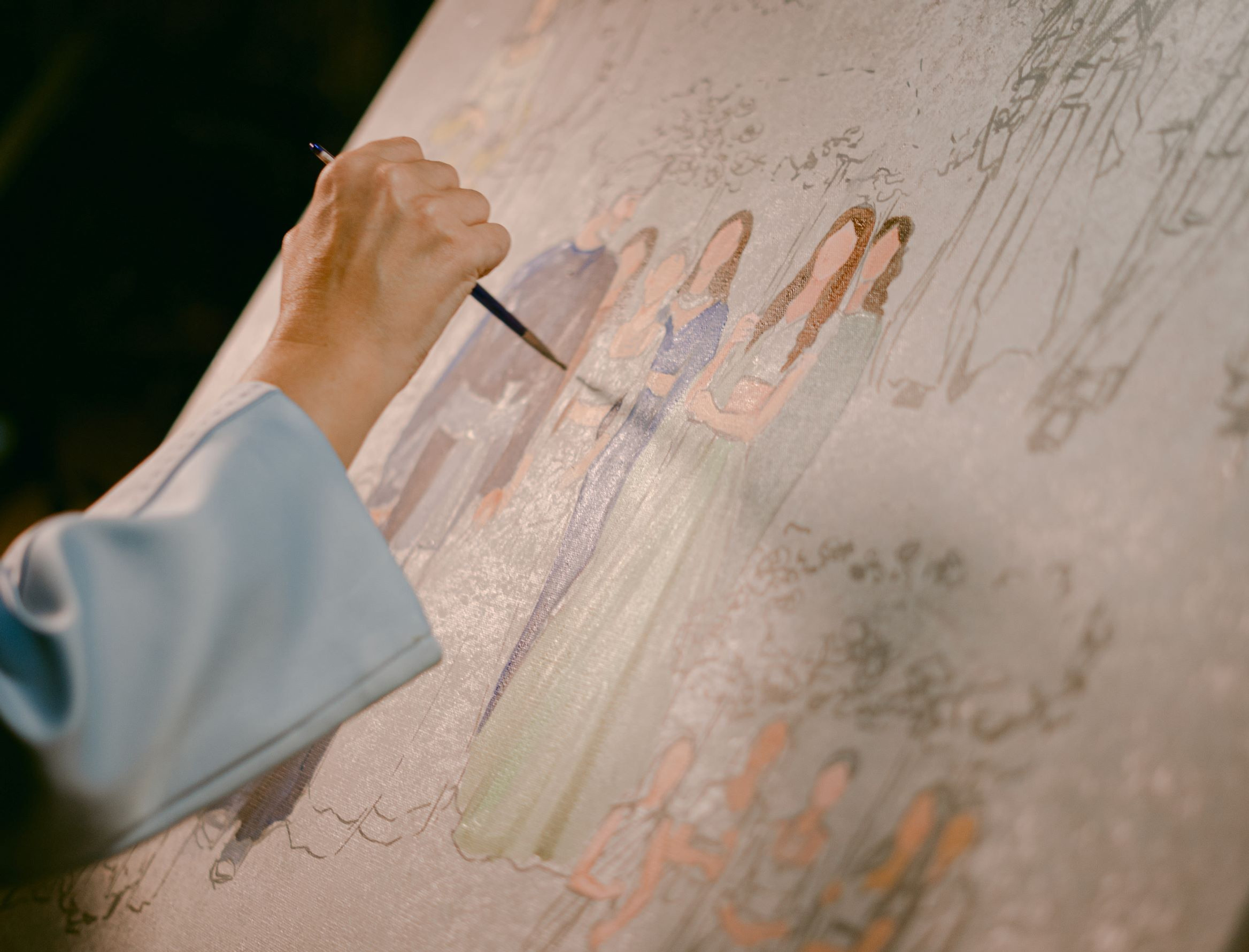 Hand painting a group portrait on a canvas easel, with sketched figures and soft pastel colors against a dark studio background.