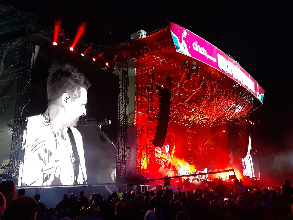 Large outdoor concert stage illuminated in red, viewed from the audience at The Isle of Wight Festival.