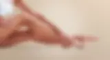 Woman sitting and gently touching her smooth, hair-free legs, highlighting results after electrolysis hair removal treatment with a neutral background