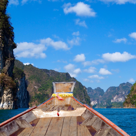 A wooden boat glides through the waters of Khao Sok National Park, Thailand.