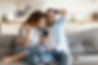 A man with a beard, white t-shirt, blue long sleeved button up shirt, sleeves rolled up sitting on a couch in a home with a soman next to him, her head resting against his check. The man and woman are laughing. This represents the need for couples counseling katy, tx and couples therapy katy, tx 77494. This also represents the need for couples therapist katy, tx and couples counselor katy, tx 77494.