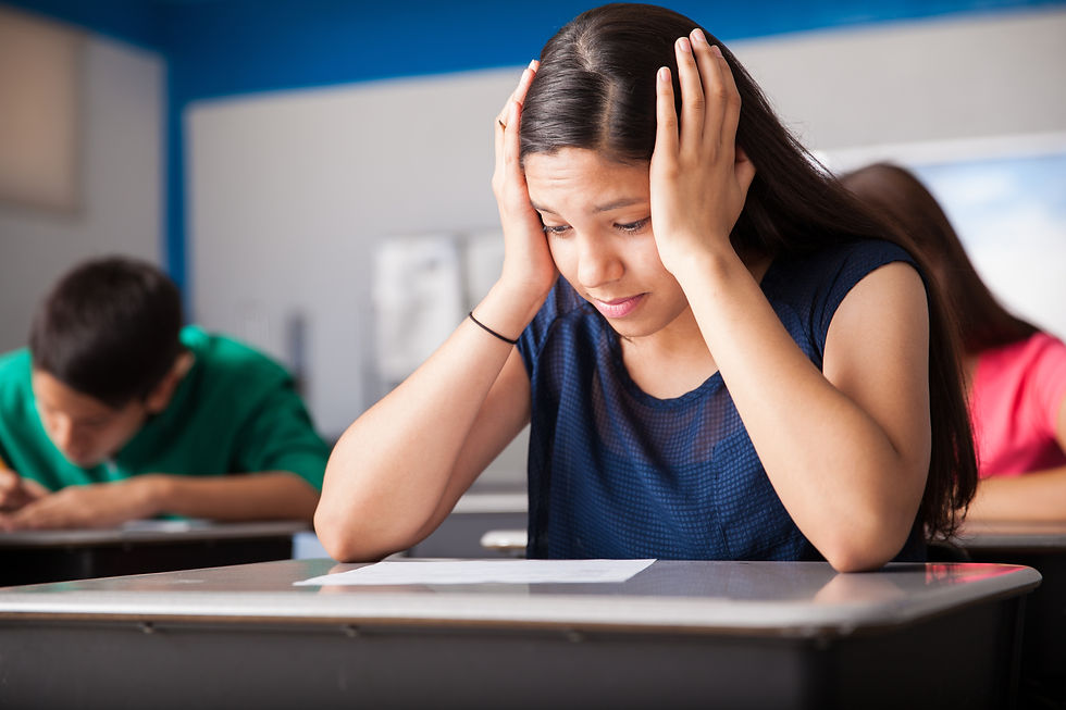 Teen sitting at school desk hands on side of head looking anxious. Represents teen anxiety and need for teen anxiety therapy katy tx or teen anxiety counseling in katy tx. Also represents the need for neurofeedback for anxiety katy texas.