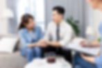 An Asian couple sitting on a couch, holding hands, smiling at each other with a woman holding a clip board and a pen sitting across from them. This represents the need for marriage counseling katy, tx 77494. This also represents the need for a marriage counselor katy, tx and a marriage therapist katy, tx 77494.