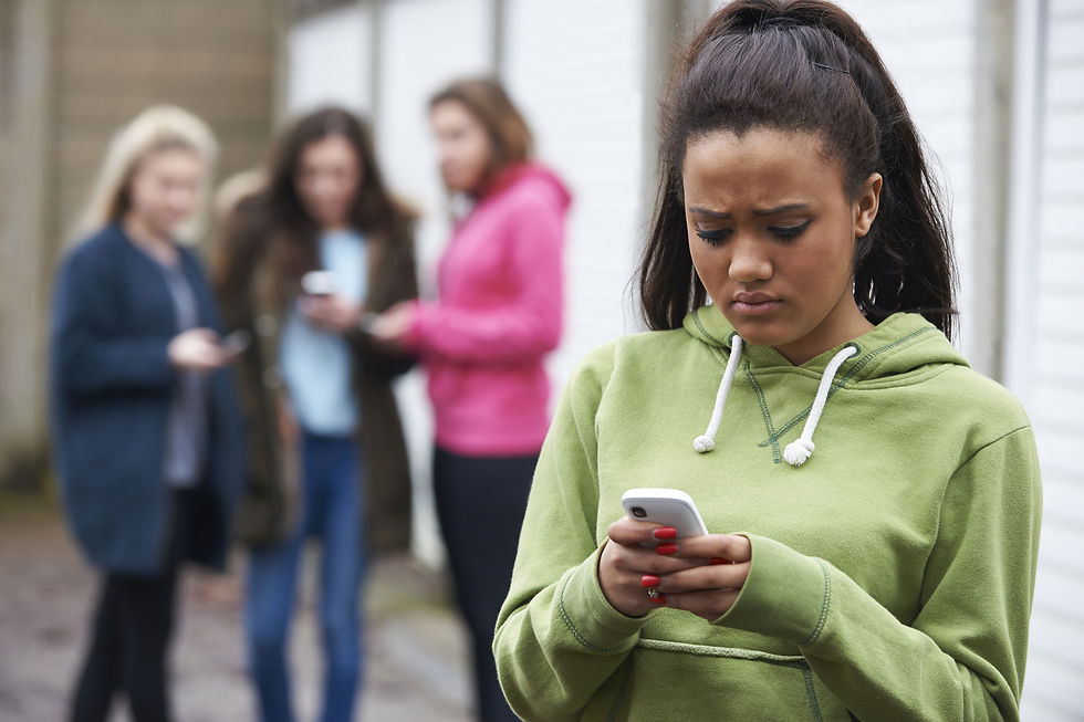 An African American teenage girl, wearing a green hoodie, looking at her phone, looking sad with a group of girls behind her, looking at their phones and at the girl. This represents the need for therapy for ptsd in katy, tx and counseling for PTSD katy texas 77494. This also represents the need for family therapy and teen counseling katy, tx 77494.
