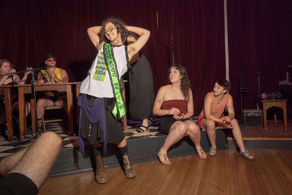 Winner Thistle Pernot poses onstage wearing the Hudson Valley’s Sexiest Armpit 2026 sash at Unicorn Bar