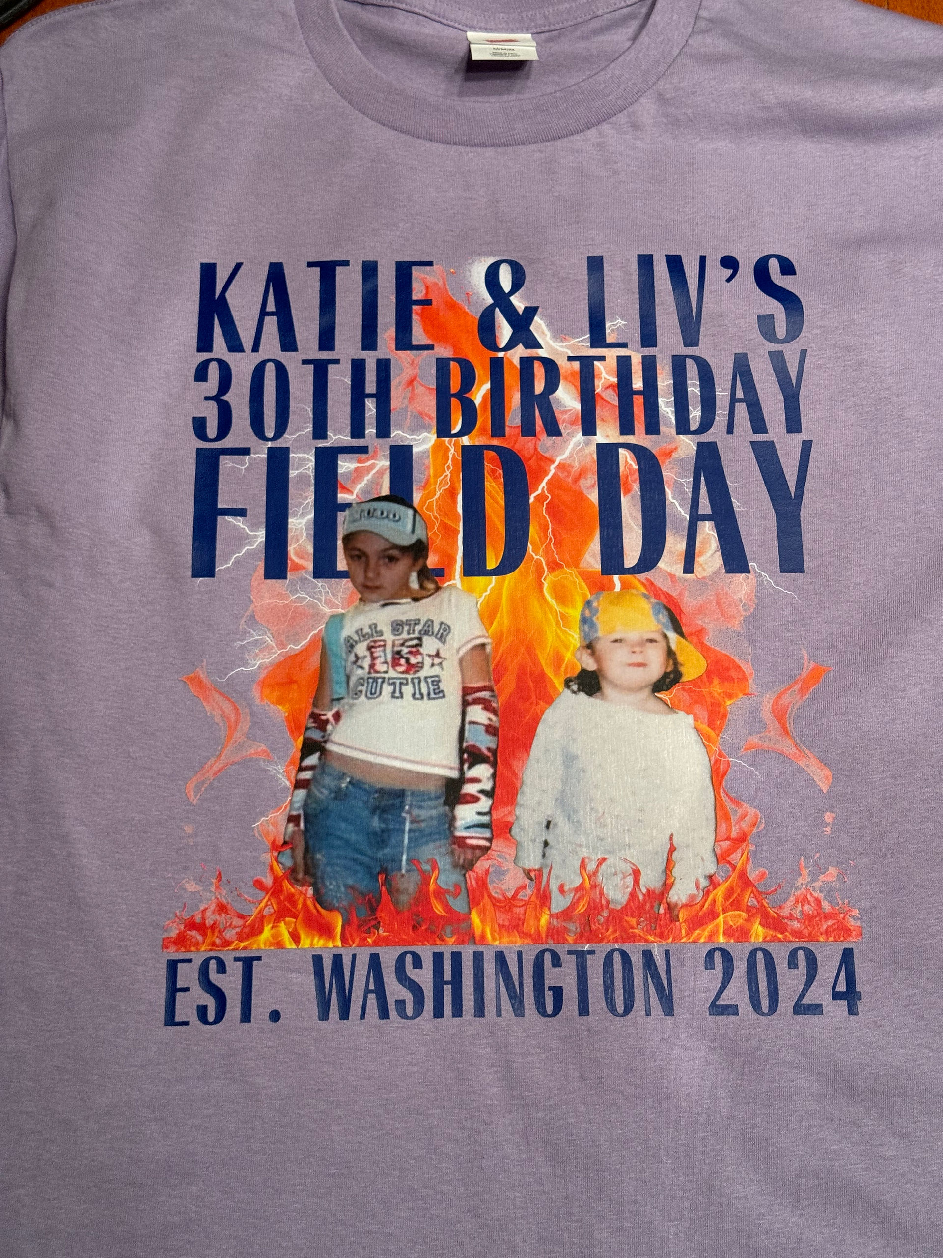Lavender shirt with navy text "Katie & Liv's 30th Birthday Field Day, Est. Washington 2024" and a graphic of two young girls in silly outfits, coming out of flames