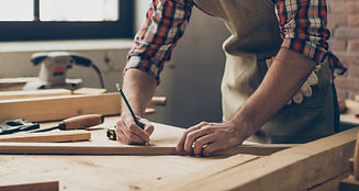 Bearded handsome cabinetmaker at the tabletop with pencil drawing sign on plank. Stylish craftsman