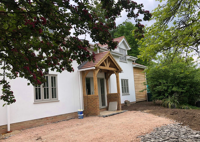 Completed self-build house front elevation with silicone based render, wood cladding, oak front porch, dormer roof window.