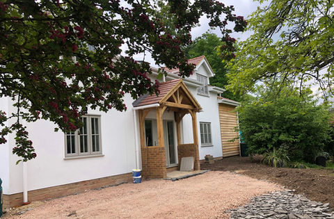 Completed self-build house front elevation with silicone based render, wood cladding, oak front porch, dormer roof window.
