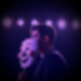 a person holding a happy mask close in front of their face, with the spotlight on them on 