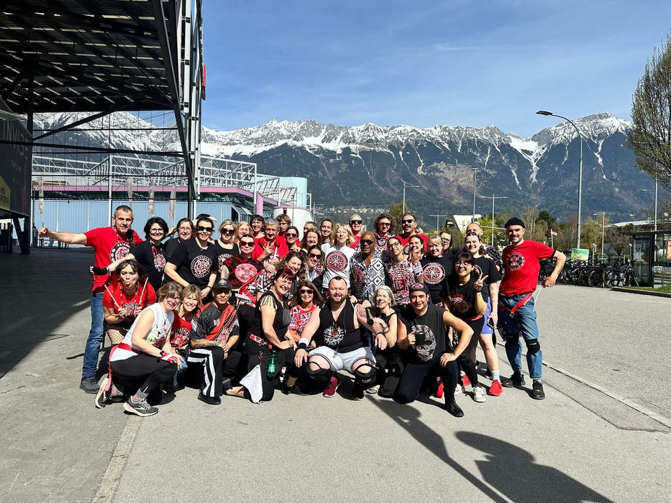 Group of Batala players posing in front of Austrian mountains in the daytime