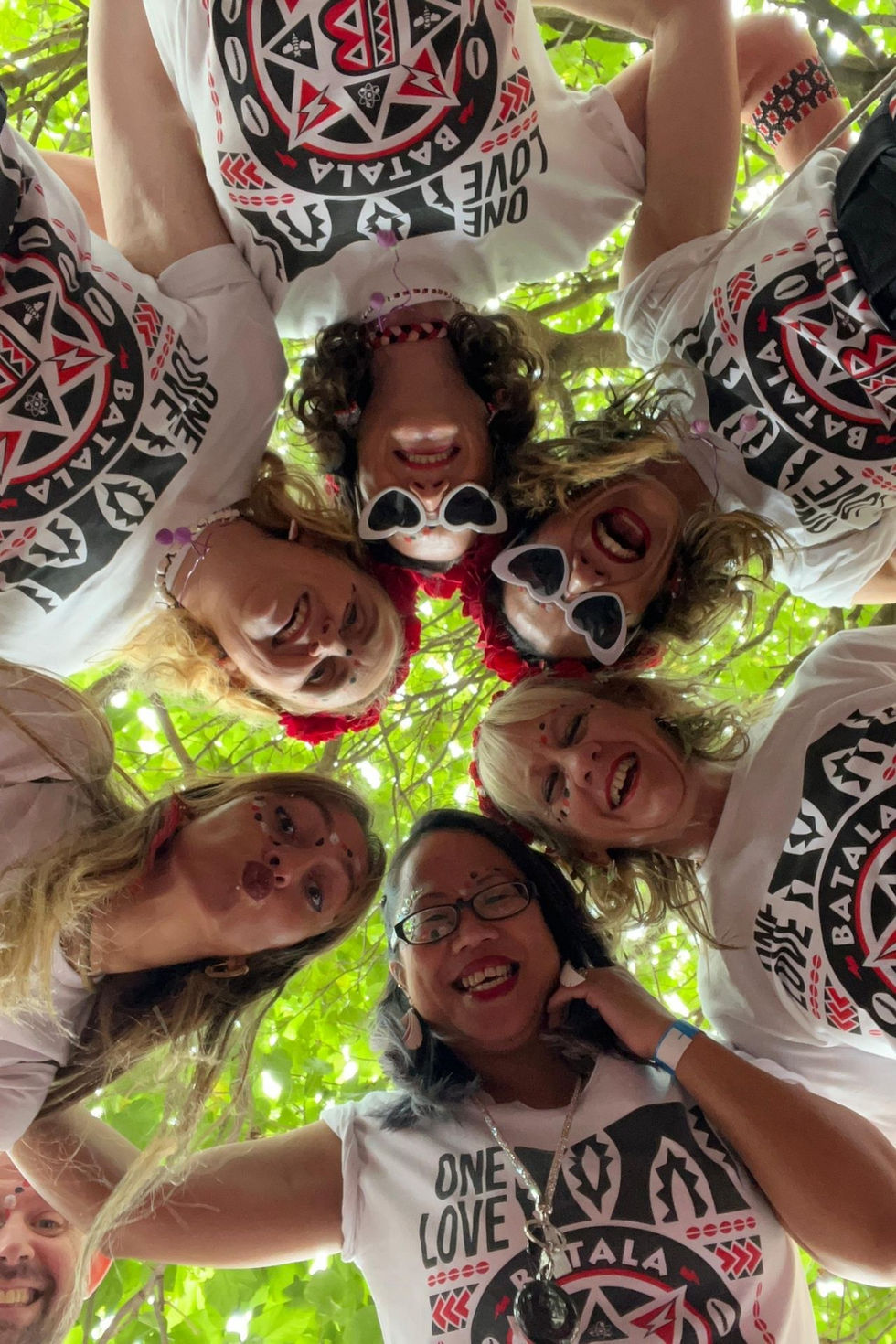 Batala Manchester players in a circle looking down into the camera with trees above them