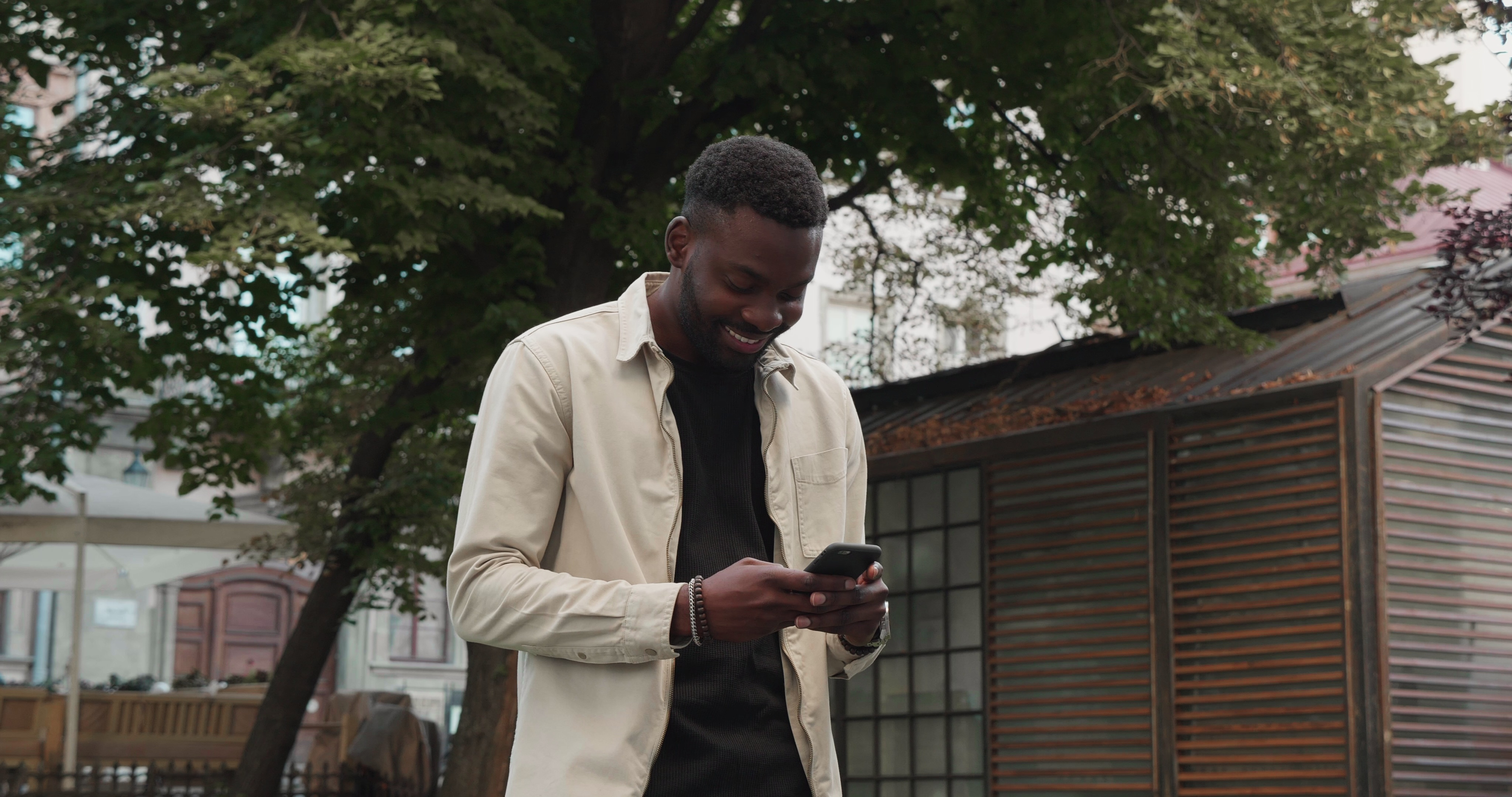atractive-afro-american-man-walking-down-the-street-and-typing-message-on-phone-wears--SBI