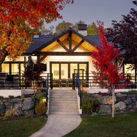 Lakeside elevation at twilight in Lake of the Pines, with timber gable, terraced rock walls, and maples