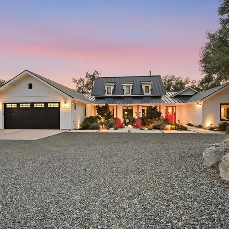 White modern farmhouse custom home in Loomis, California, at twilight with black garage doors and a dormered metal roof