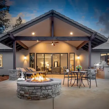 Covered patio with a timber gable, stone fire pit and outdoor kitchen at dusk in The Alpine