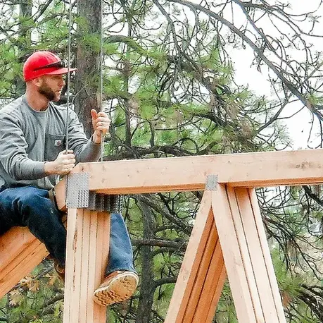 Carpenter setting a timber truss on a pavilion frame among the pines