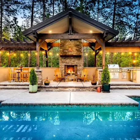 Poolside pavilion with a stone fireplace, pergolas and built-in grill among the pines