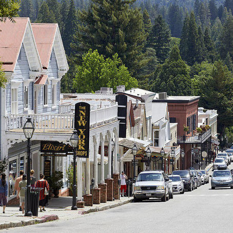 Historic Gold Rush storefronts and Victorian buildings lining Broad Street in downtown Nevada City, California, with pine-covered hills rising behind the town.
