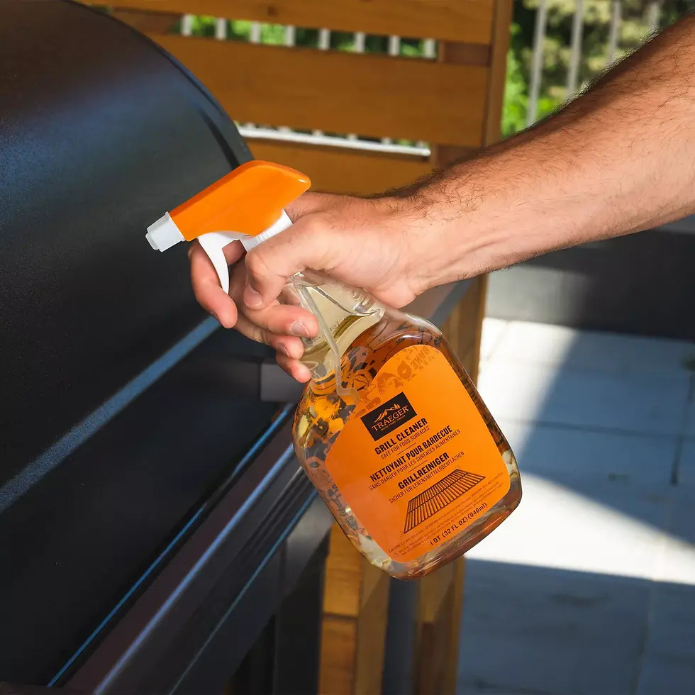 Hand holding Traeger grill cleaner spray next to a pellet grill