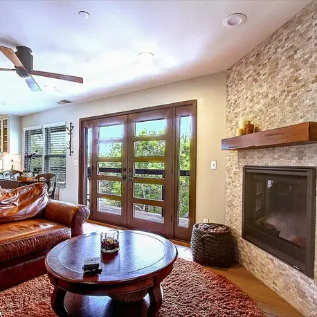 Remodeled living room with a stacked-stone fireplace and timber mantel