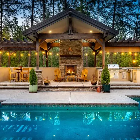 Poolside pavilion with a stone fireplace, pergolas and built-in grill in Meadow Vista, CA
