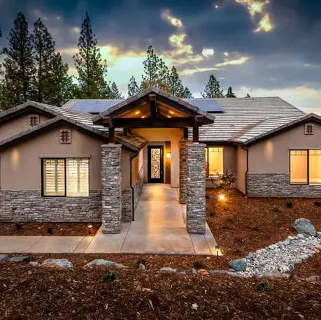 The Alpine custom home lit at dusk with stone entry columns in Winchester Country Club, Meadow Vista