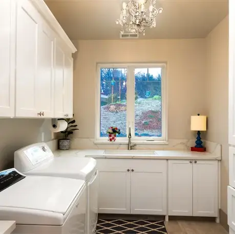 Laundry room with white cabinetry, a utility sink and chandelier in an Auburn custom home