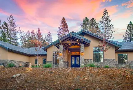 The Motherlode semi-custom home at sunset with a timber entry gable and stone columns