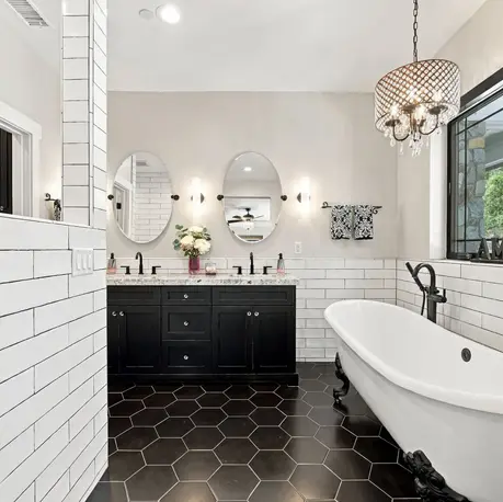 Primary bath with black clawfoot tub, double vanity, oval mirrors, and beaded chandelier