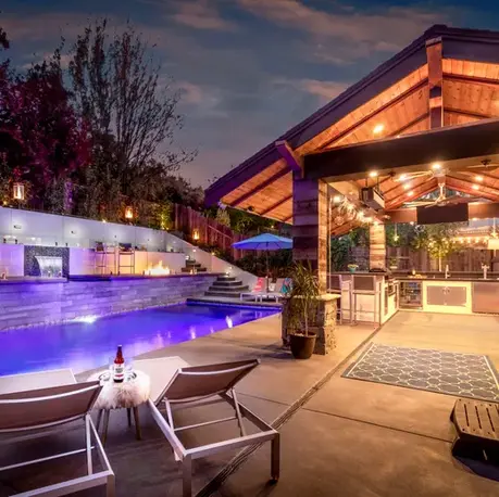 Pool and covered outdoor kitchen pavilion lit at dusk on a foothill property