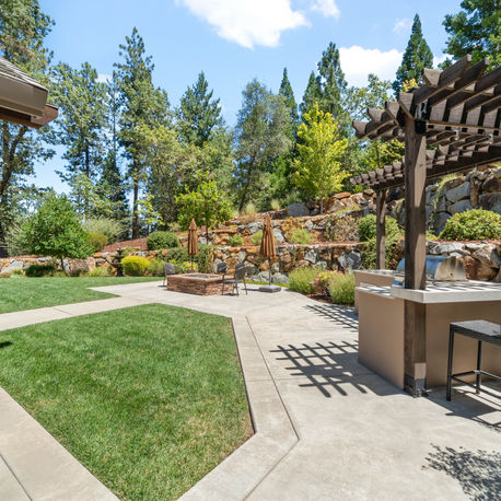 Backyard lawn with a pergola bar and boulder retaining wall at The Ridge
