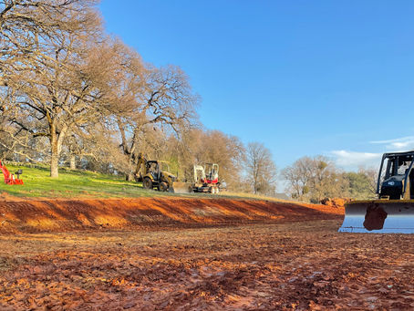 Foothill excavation on a sloped Placer County lot with red clay soil, oak trees, and grading equipment