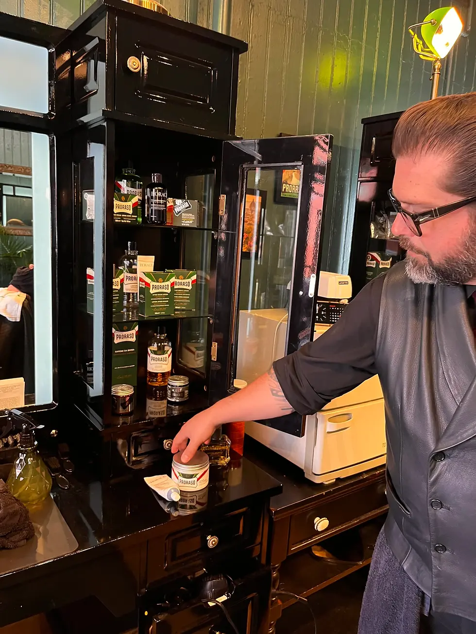 Barber selecting styling product at a vintage grooming station inside Barbery Coast barber shop in San Francisco.
