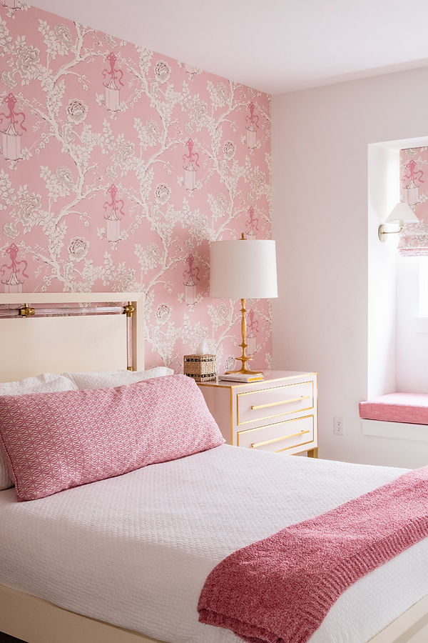 Pink bedroom with wallpaper and bed with side table and lamp.