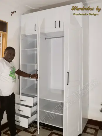 Three white door hinged wardrobe with closed in shelves and a closed in hanging section for clothes designed by vron interior designs.