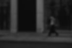 grayscale-shot-male-walking-along-pedestrian-zone-near-building 1