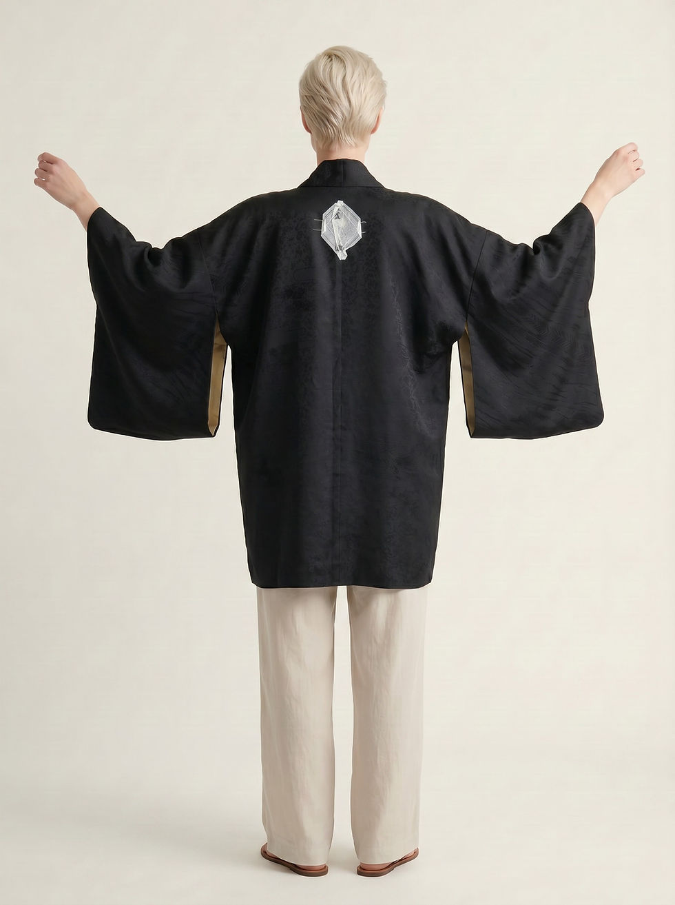 Woman wearing a vintage 1960s “new old stock” silk Kuro‑Haori with Kyoto rinzu weave and Katabami crest, arms extended agains