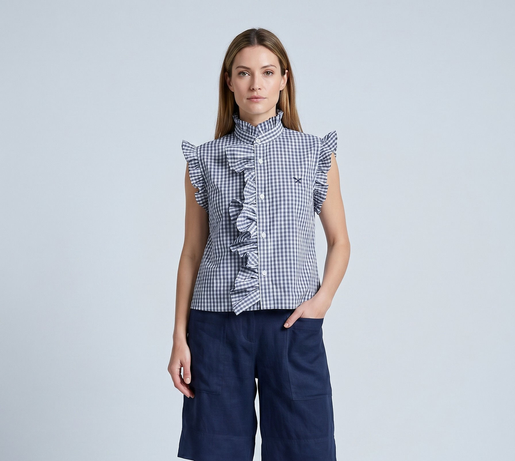 Blue gingham ruffled sleeveless blouse styled with navy knee‑length shorts.
