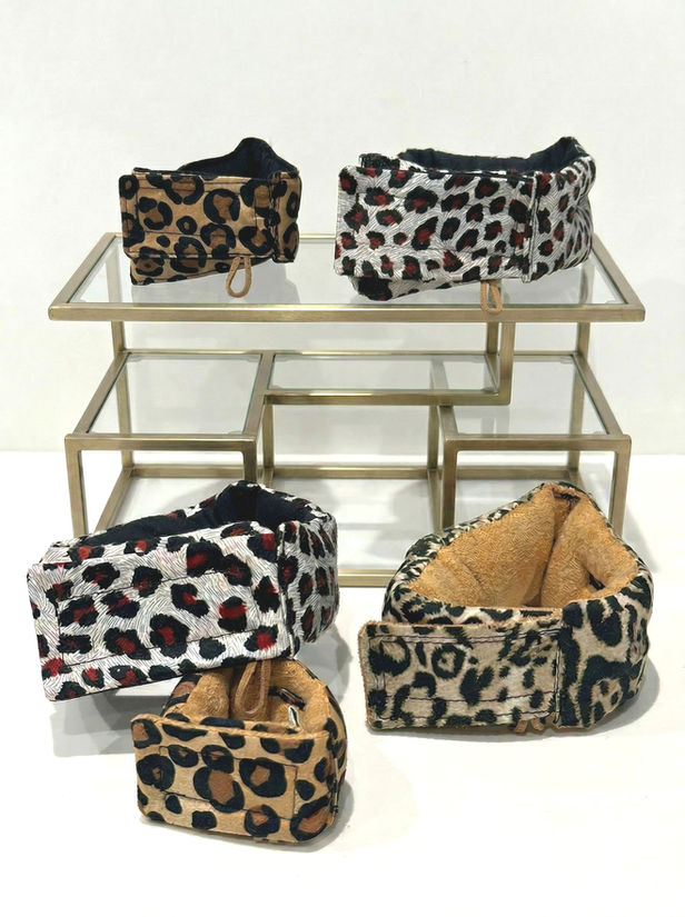 A selection of hand‑crafted animal‑print support collars arranged on a neutral background. The collars vary in size and feature bold prints and soft gradient textiles, each with a Velcro closure and soft lining designed to support an oesophagostomy feeding tube.