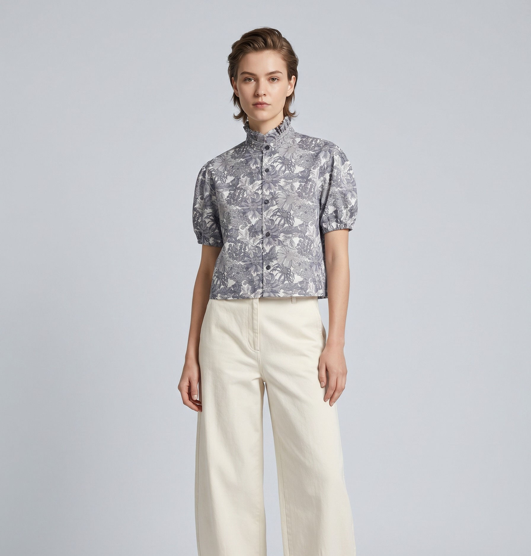 A studio fashion photograph of a model with short brown hair wearing a bespoke, semi-cropped blouse in monochrome Liberty