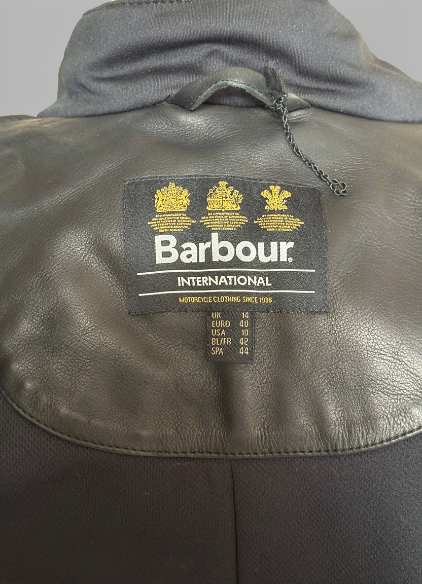 Close-up of a Barbour International label on leather featuring Triple Royal Warrant gold crests and size UK 14.