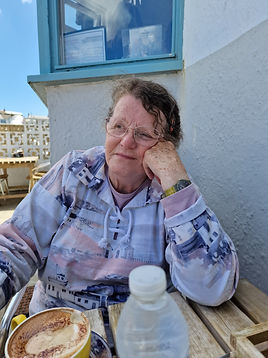 Photo of Susan MacPherson, the artists mother. Sitting at a table, resting her head on her hand. Smiling in the sunshine.