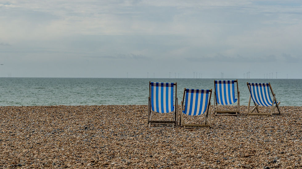 Four blue-and-white striped deck chairs on a pebble beach facing a calm sea under a cloudy sky.