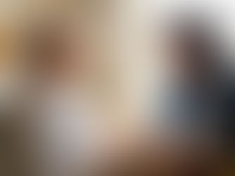 An elderly woman in bed and a younger woman share a warm smile by a window. Colourful blanket on lap. Cosy mood.