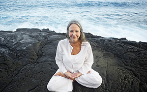 A woman sitting on a large rock by the ocean